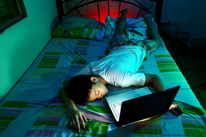 man lying in bed asleep laptop still running playing game late into the night